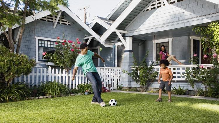 Father 和 son playing soccer on the front lawn while mom watches from the porch. 